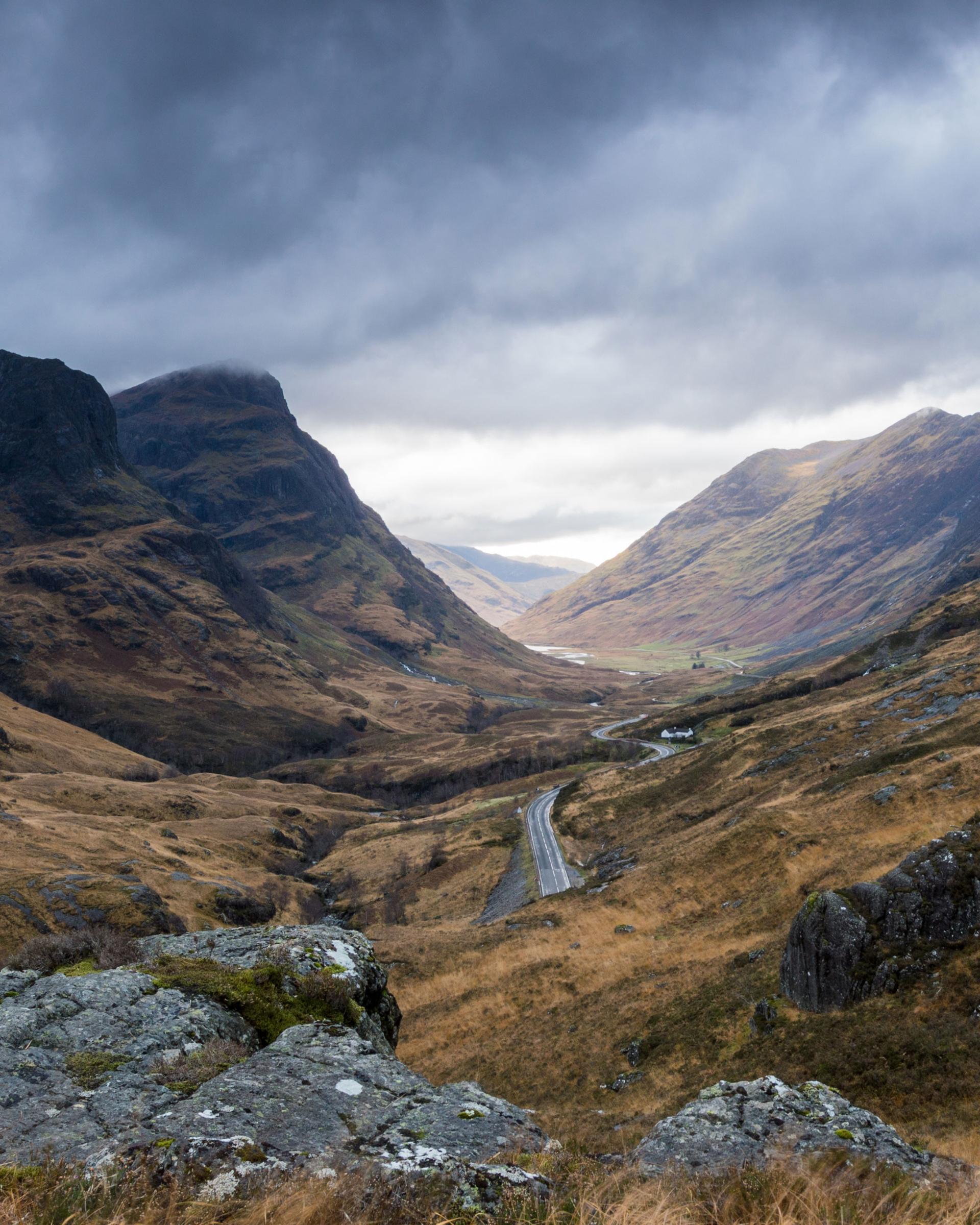 A road winding through a steep mountain valley beneath low cloud.